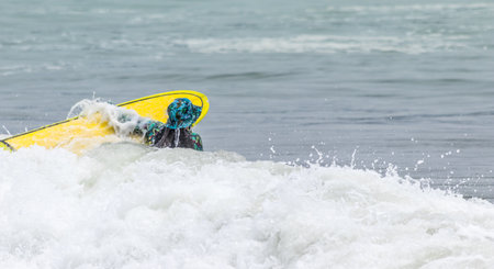 A back shot of a girl with a summer hat holding a yellow skateboard bear the gray seawater