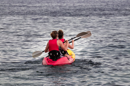 A back view of two athletic women kayaking on the wavy seaの写真素材