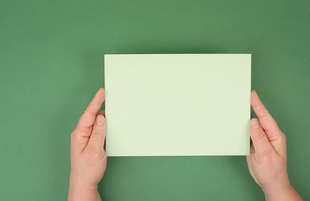 Holding empty paper in the hands, green colored background, copy space for text, blank card