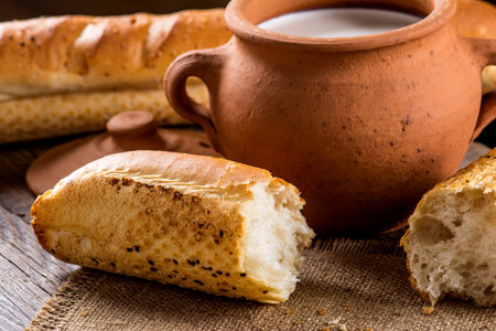 A closeup of a Clay pot with milk and baguette on a wooden table
