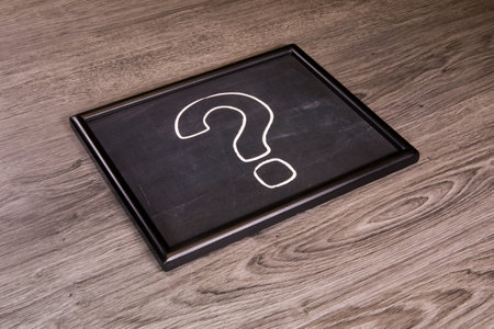 A question mark icon on chalkboard, blackboard over a gray wood backgroundの写真素材