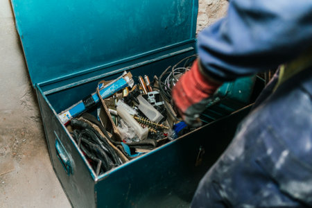 A worker in a blue uniform putting metal instruments in a messy tool boxの写真素材