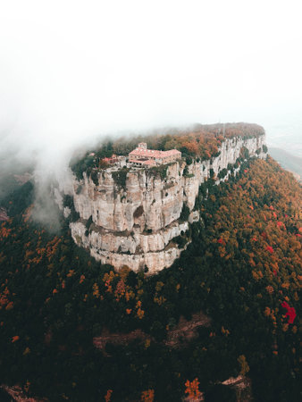 A vertical shot of the beautiful Santuario del Far in La Garrotxa, Catalunya with fog around itの写真素材