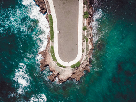 An aerial view of a road near rocky cliffs with waves splashing