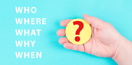 The words who, what, why, when, where are standing on a blue colored background, hand is holding a...