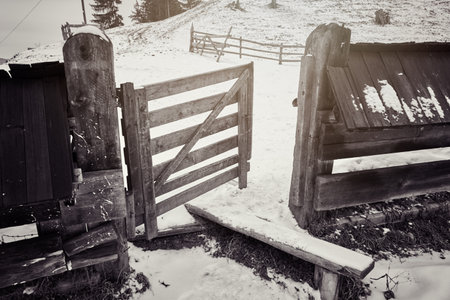 A grayscale shot of an old wooden fence and gate in a rural landscapeの写真素材