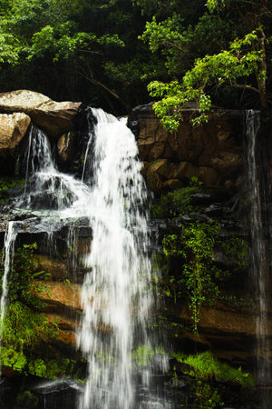 A vertical shot of the beautiful waterfall surrounded by rocks and green vegetation.
