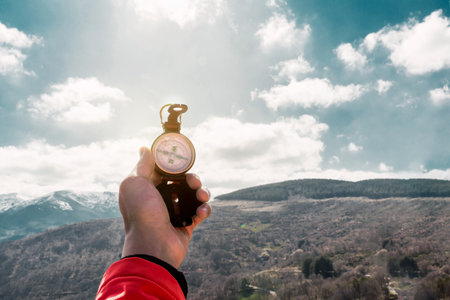 A closeup shot of a compass in a man's hand with mountain and cloudy sky in background