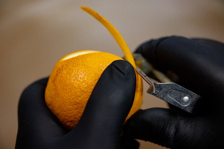 A closeup of hands wit6h black gloves peeling an orangeの写真素材
