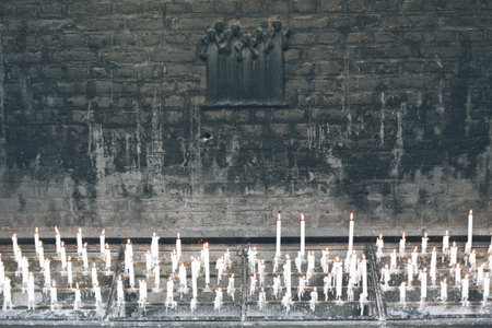 A high angle shot of a religious site with burning candles next to a gray wallの写真素材