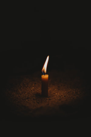 The small candle burning on the soil ground in the dark - light contrast conceptの写真素材