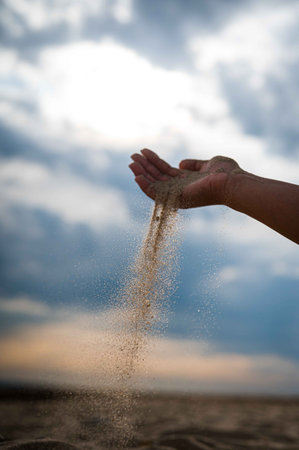 A vertical shot of a hand pouring sand on a beachの写真素材