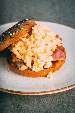 A vertical closeup shot of a gourmet scrambled egg sandwich bagle on a plateの写真素材