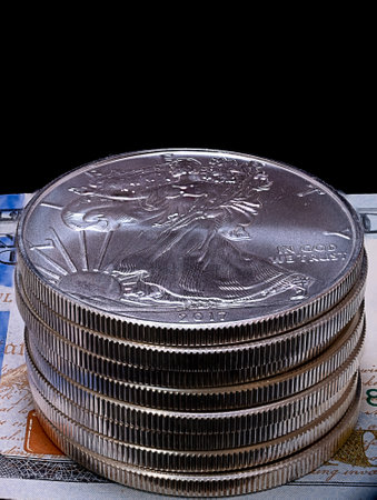 Vertical macro shot of the stack of U.S. Silver Eagle bullion coins laying on top of a hundred...