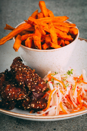 A vertical shot of sweet potato fries, teriyaki chicken strips, and saladの写真素材