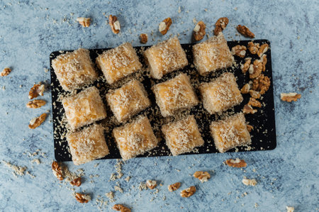 A top view of delicious baklavas on a black cutting board with nuts on a concrete background