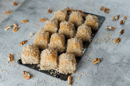 A closeup of delicious baklavas on a black cutting board with nuts on a concrete background