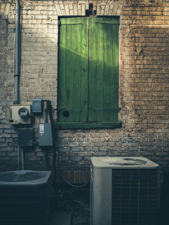 A vertical shot of old air conditioners by a stone wall with green wooden doors