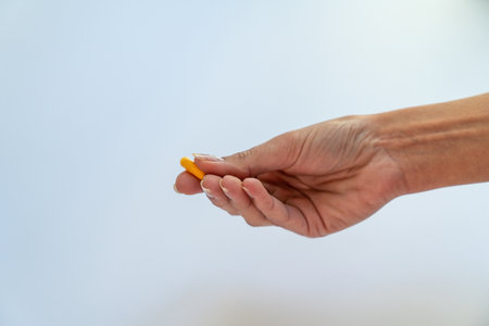 A hand holding a yellow pill on a white backgroundの写真素材