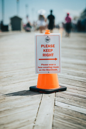 A vertical shot of a sign on an orange cone in the middle of a pathway