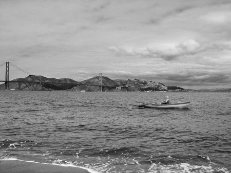 A black and white shot of a fisherman on a boat in San Francisco and the Golden Gate in the back
