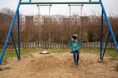 A closeup of a young boy and teddy bear sitting on a swing set at a playground in the Jan Pawla parkの写真素材