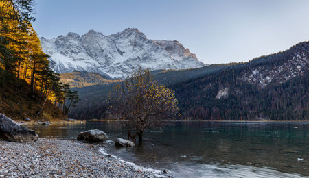 A landscape of a lake surrounded by a forest and rocky hills covered in the snow in winter