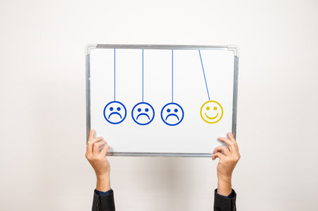 A Newtonâ€™s cradle style 3 blue frowning emojis with one smiling emoji held by a person from...