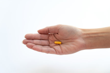 A hand holding a yellow pill on a white backgroundの写真素材