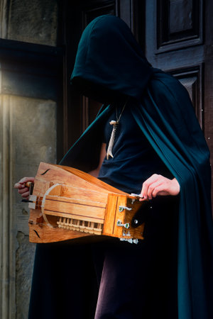 A closeup of a man in a cloak holding a hurdy gurdy medieval instrument