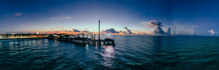 A panoramic shot of a bridge in the sea under a cloudy sky with sunsetの写真素材