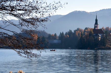 A scenic shot of a church surrounded by a lake, a forest, and mountains in Slovenia