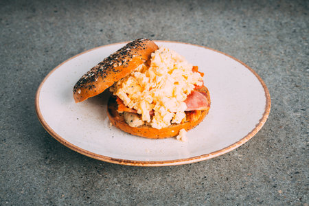 A closeup shot of a gourmet scrambled egg sandwich bagel on a plateの写真素材