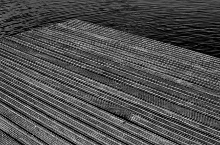 A greyscale shot of a wooden pier in a sea