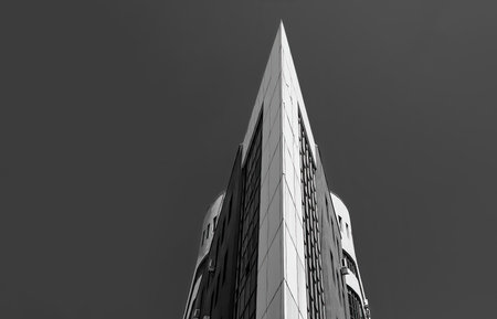 A grayscale shot of a corner of a high modern building against a cle sky on a sunny dayの写真素材
