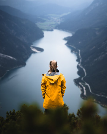 A young woman wearing a yellow coat and standing on a hill surrounded by a river on a gloomy dayの写真素材