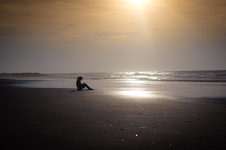 A silhouette of a person sitting on a beach during a sunny dayの写真素材