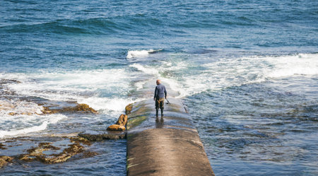 A fisherman standing on a pier and looking at rough sea