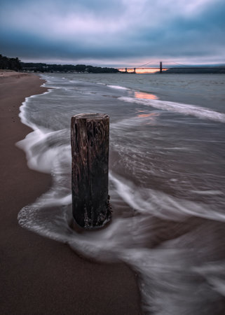 An old wooden bollard at a shore with sunset sky in the horizon