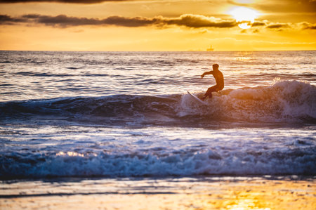 A shot of Caucasian male surfing the ocean waves with the background of yellow sunsetの写真素材