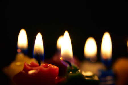 A closeup shot of colorful candles burning in the darkness on a blurred backgroundの写真素材