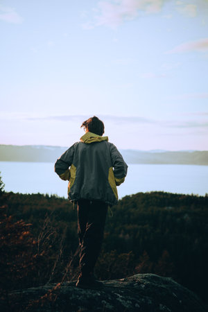 A vertical shot of a person standing on a rock by the sea at sunsetの写真素材