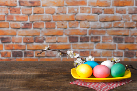 A blossomed twig with multi-colored Easter eggs in the rustic background with a copy space