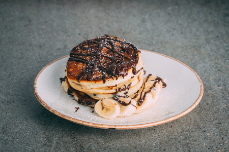 A Closeup of pancakes with chocolate and bananas served on a white plateの写真素材