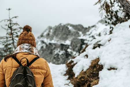 ACaucasian female hiker wearing winter clothes and a backpack walking on a snowy path in the forestの写真素材