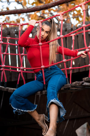 A vertical shot of a White lady wearing a turtleneck and jeans posing behind a playground netの写真素材