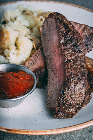 A Smashed potato served with a piece of meat and red sauce on a white plateの写真素材