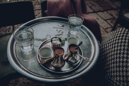 A closeup of cezves with hot coffee on a tray on the table with water glasses on itの写真素材