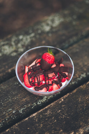 A vertical shot of a pudding with whipped cream and strawberries on a wooden tableの写真素材