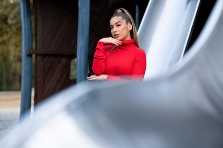 An attractive White lady wearing a red turtleneck posing sitting on a playground slideの写真素材